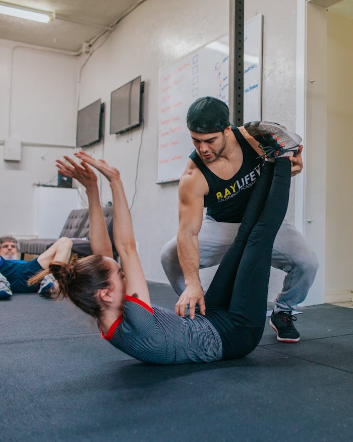 about-07 Personal trainer helping a woman with flexibility exercises in a gym setting.