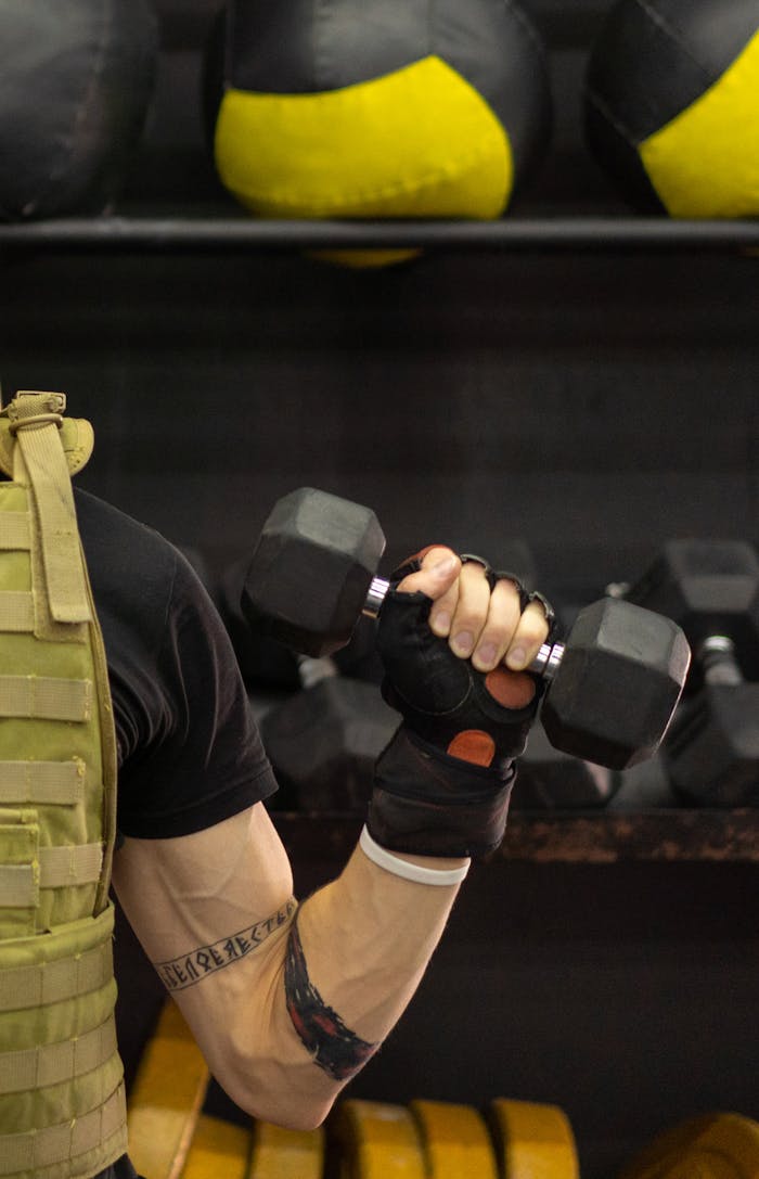 Side view of a person lifting a dumbbell while wearing a weighted vest in a gym.